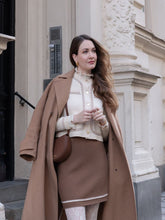 A lady wears a white cardigan and a skirt.